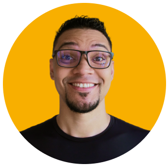 Foto de Mayk Brito sorrindo, usando óculos e camixa preta, barba e fundo amarelo